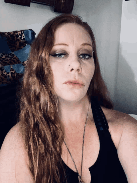 a woman with red hair is wearing a black tank top and a silver necklace