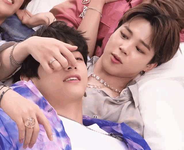a man wearing a necklace that says chanel is laying on another man 's lap