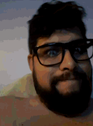 a man with glasses and a beard looks at the camera with his eyes closed