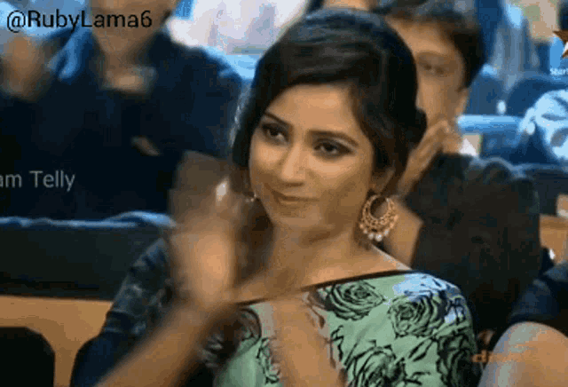 a woman in a green and black floral top is clapping her hands