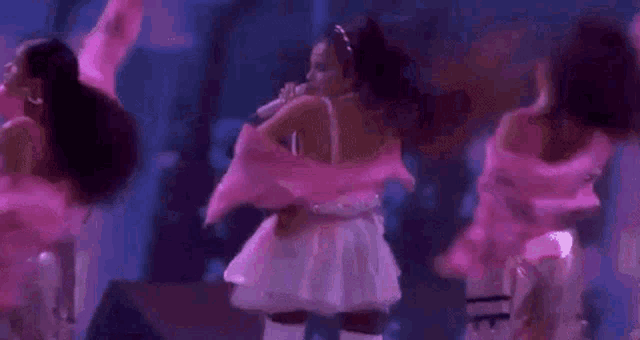 a woman in a pink jacket and white skirt is singing into a microphone while dancing on a stage .