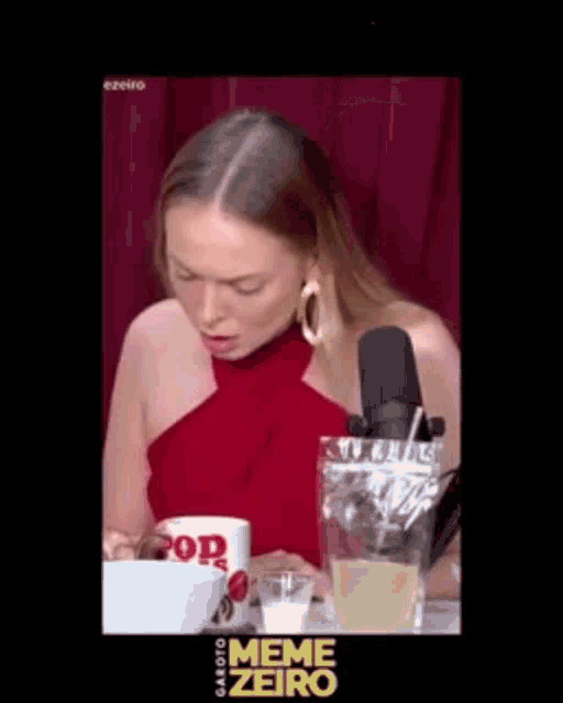 a woman in a red dress is sitting at a table with a microphone and a bowl of popcorn .