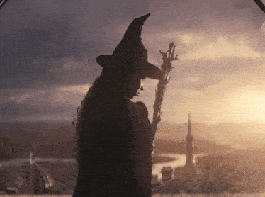 a woman in a witch hat holds a wand in front of a sunset