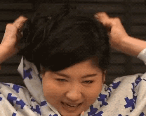 a woman wearing a blue and white kimono is holding her hair in a bun .