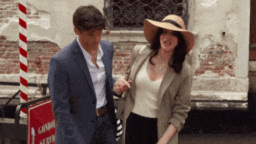 a man in a suit and a woman in a hat are walking in front of a sign that says gondola