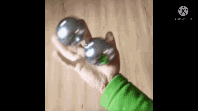 a person in a green sweater is holding two metal balls in their hands .