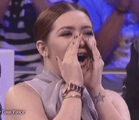 a woman with a tattoo on her wrist is laughing with her mouth open .