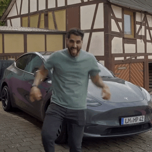 a man dancing in front of a tesla model 3 with a license plate that says lm hp 42