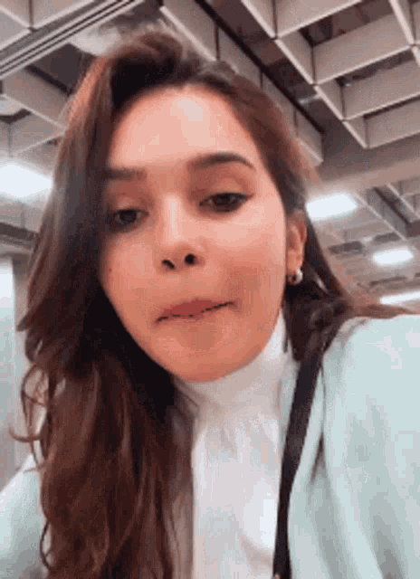 a woman wearing a white shirt and a light blue cardigan is making a face .