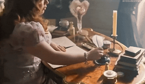 a woman is writing on a piece of paper at a table with a candle