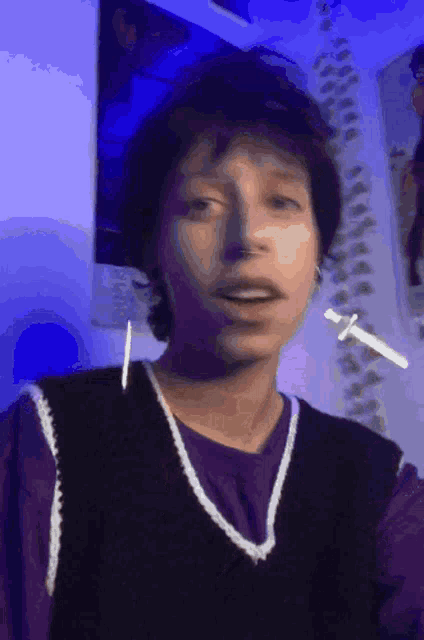 a young man wearing a purple shirt and a black vest is making a funny face