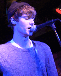 a young man singing into a microphone with a blue light behind him