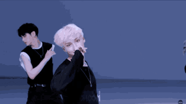 a man with white hair is pointing at the camera while another man stands behind him