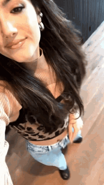 a woman in a leopard print crop top and jeans takes a selfie