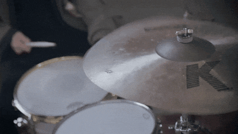 a person playing a drum set with a cymbal that has the letter k on it