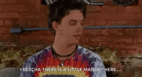 a man is sitting on a couch wearing a tie dye shirt and a necklace and talking .
