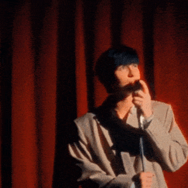 a man is standing on a stage holding a microphone in front of a red curtain .