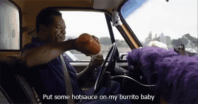 a man is sitting in the driver 's seat of a car holding a hot sauce container .