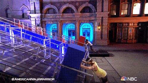 a man in a yellow shirt is pushing a large blue box on a nbc advertisement for american ninja warrior