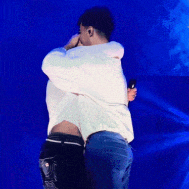 a man in a white shirt is hugging another man in blue jeans