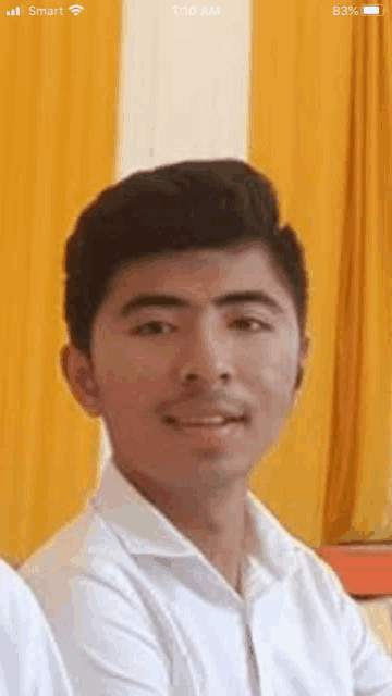 a young man in a white shirt is sitting in front of a yellow curtain and smiling .