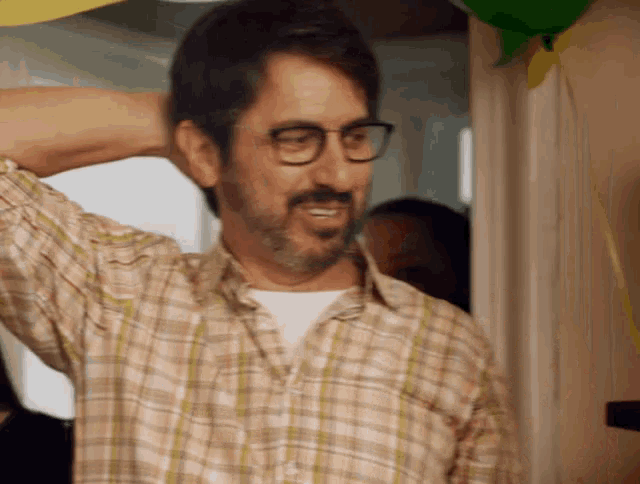 a man wearing glasses and a plaid shirt holds his hand to his head