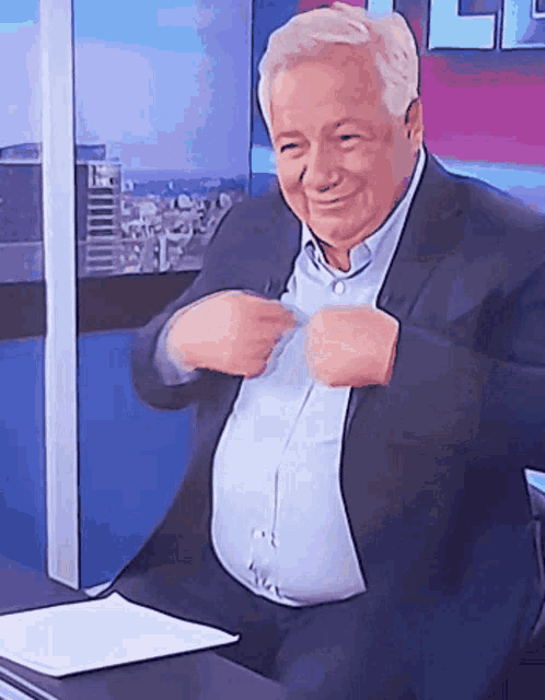 a man in a suit is sitting at a desk with his hands on his chest