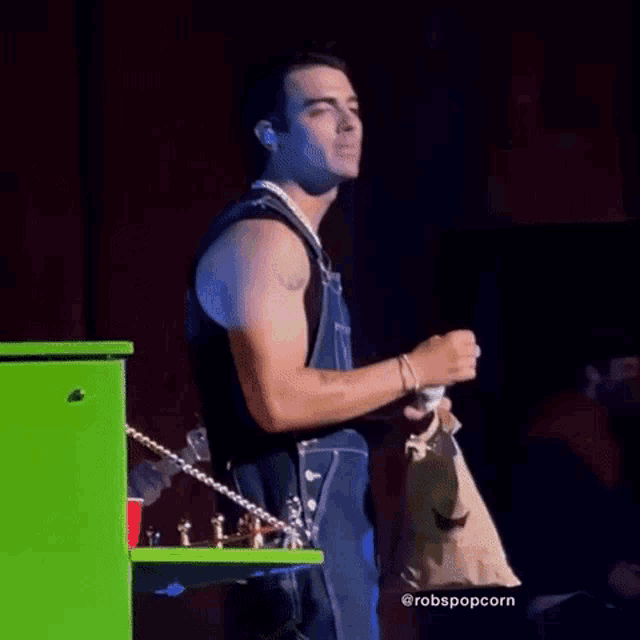 a man in overalls is singing into a microphone on a stage while holding a bag of popcorn .