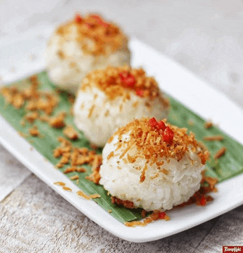a white plate topped with three rice balls with a red pepper on top .