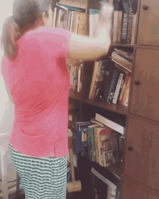 a woman in a pink shirt is standing in front of a bookshelf full of books one of which is titled bible