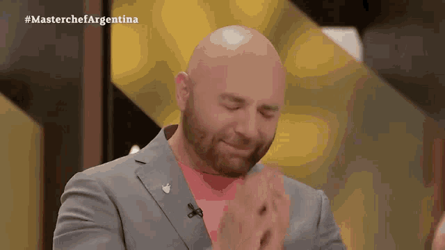 a bald man with a beard applauds in front of a masterchef argentina sign