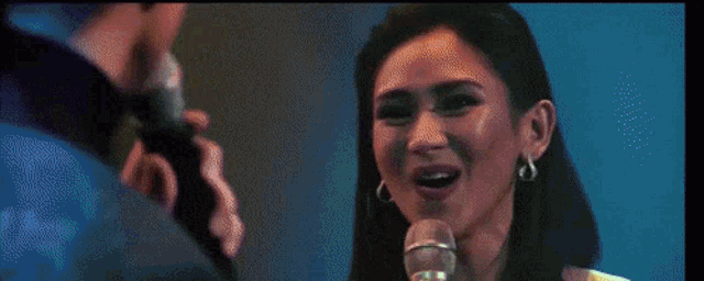 a woman is singing into a microphone with a man behind her .