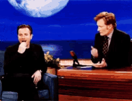 two men are sitting at a table talking to each other with a planet in the background