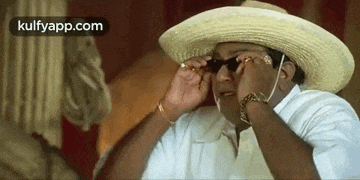a man wearing a hat and sunglasses is looking through his sunglasses .