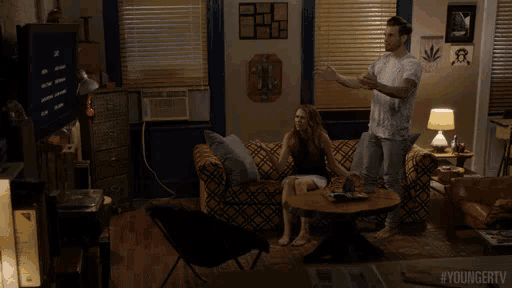 a man and a woman sitting on a couch in a living room with #youngertv written on the bottom of the screen