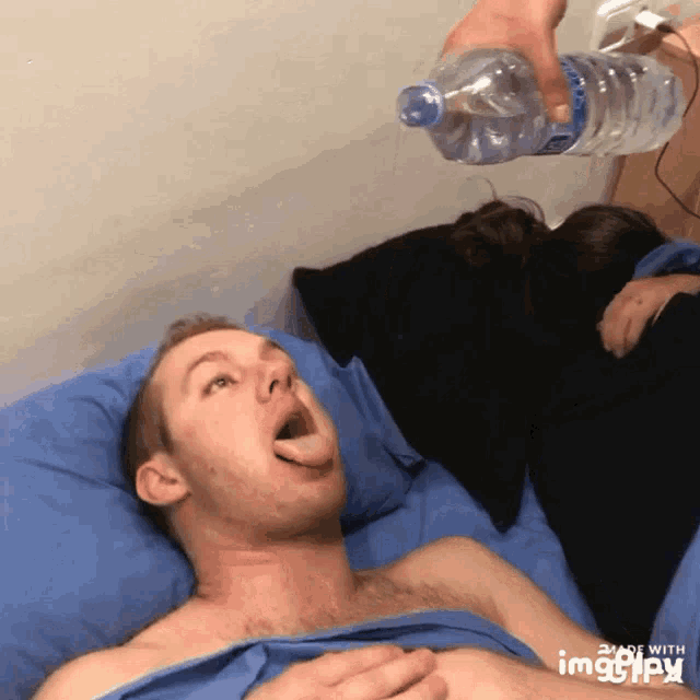 a man is laying in bed with his mouth open and a bottle of water is being poured on him