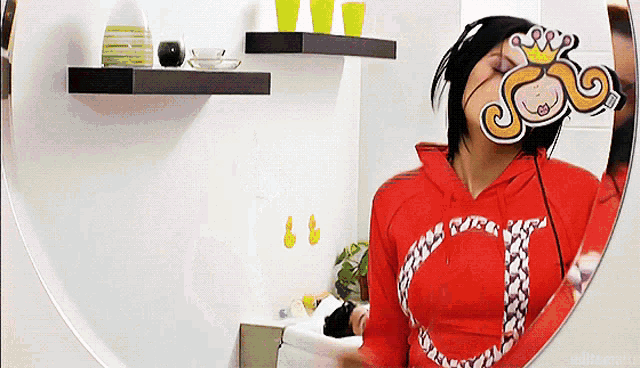 a woman in a red sweatshirt is looking at herself in a round mirror