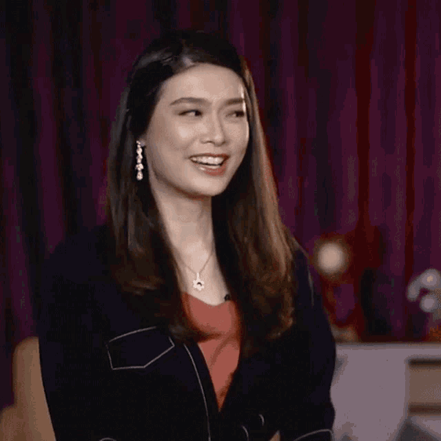 a woman is laughing with her mouth open and wearing a necklace and earrings .