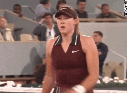 a woman in a maroon nike tank top is standing on a tennis court in front of a crowd of spectators .
