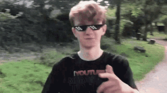 a young man wearing sunglasses and a black shirt with the word youtube on it is pointing at the camera .