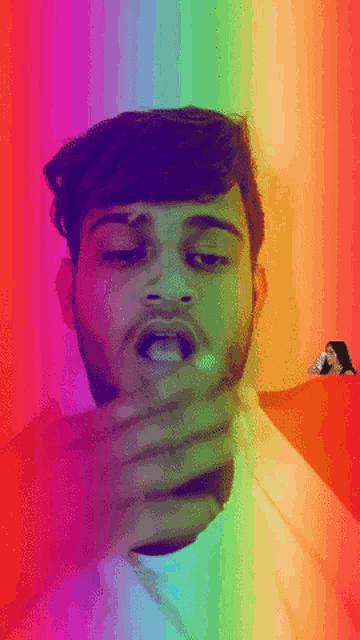 a man covering his mouth with his hand with a rainbow background behind him