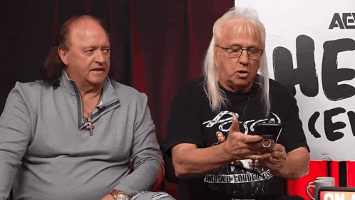 two men sitting in front of a sign that says ae on it
