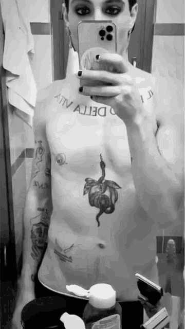 a man without a shirt is taking a selfie in a bathroom with his phone .