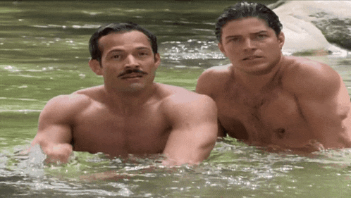 two shirtless men are swimming in a river together