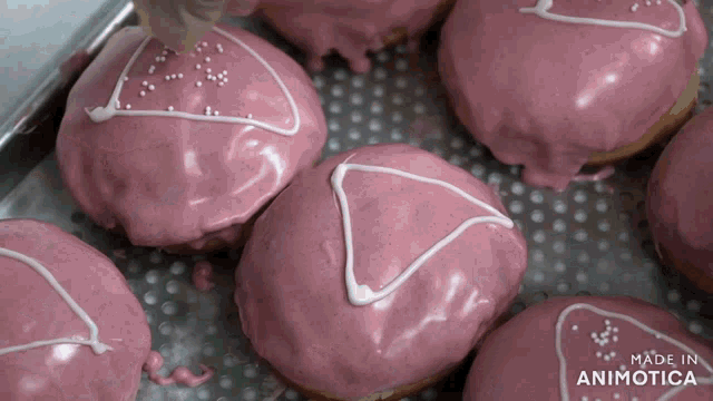 a bunch of donuts with pink frosting and white sprinkles are on a tray that says made in animatica