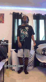 a man in a black shirt and white shorts is standing in a room next to a laundry basket .