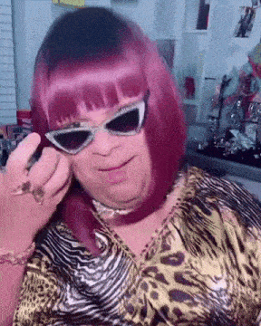 a woman with pink hair is wearing sunglasses and a leopard print shirt .
