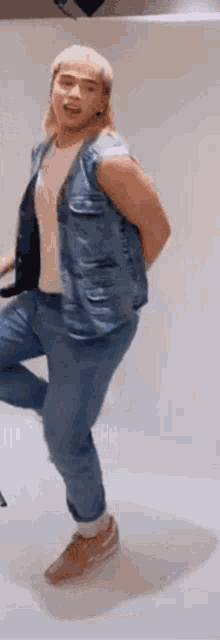 a man wearing a denim vest and jeans is dancing on one leg .