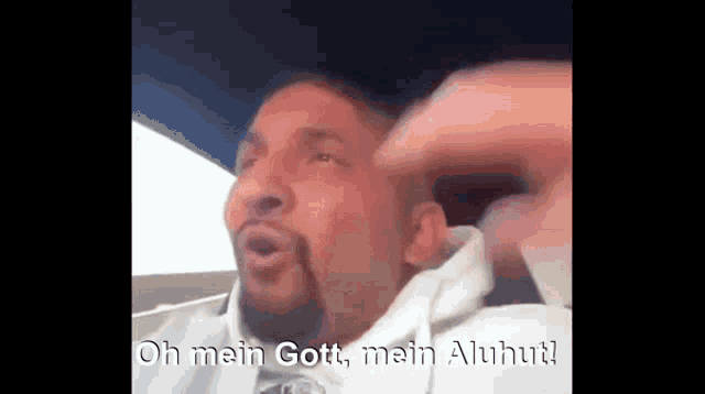 a man with a beard is sitting in a car and says oh mein gott mein aluhut !