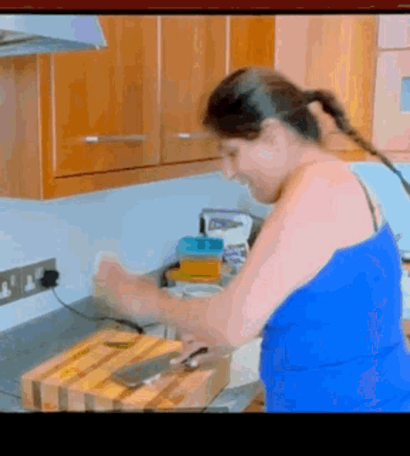 a woman in a blue tank top is cutting vegetables on a cutting board